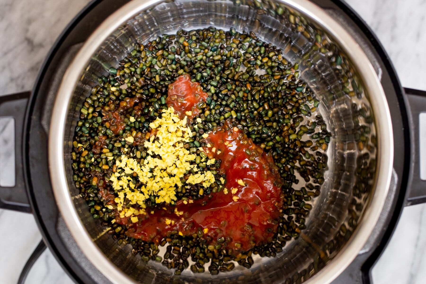 black gram, spices and ginger being added to an instant pot