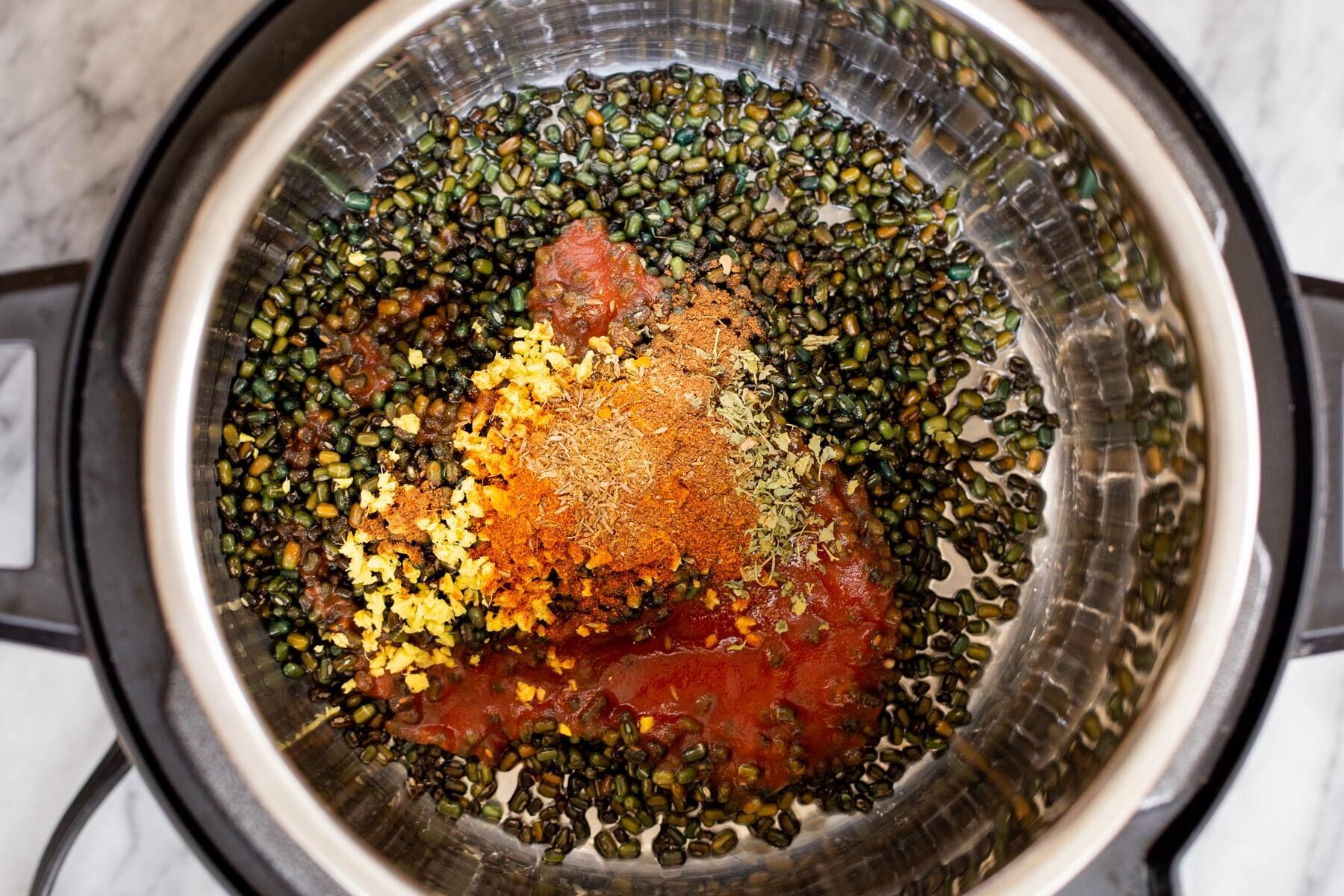 black gram being added to an instant pot along with spices and tomato paste