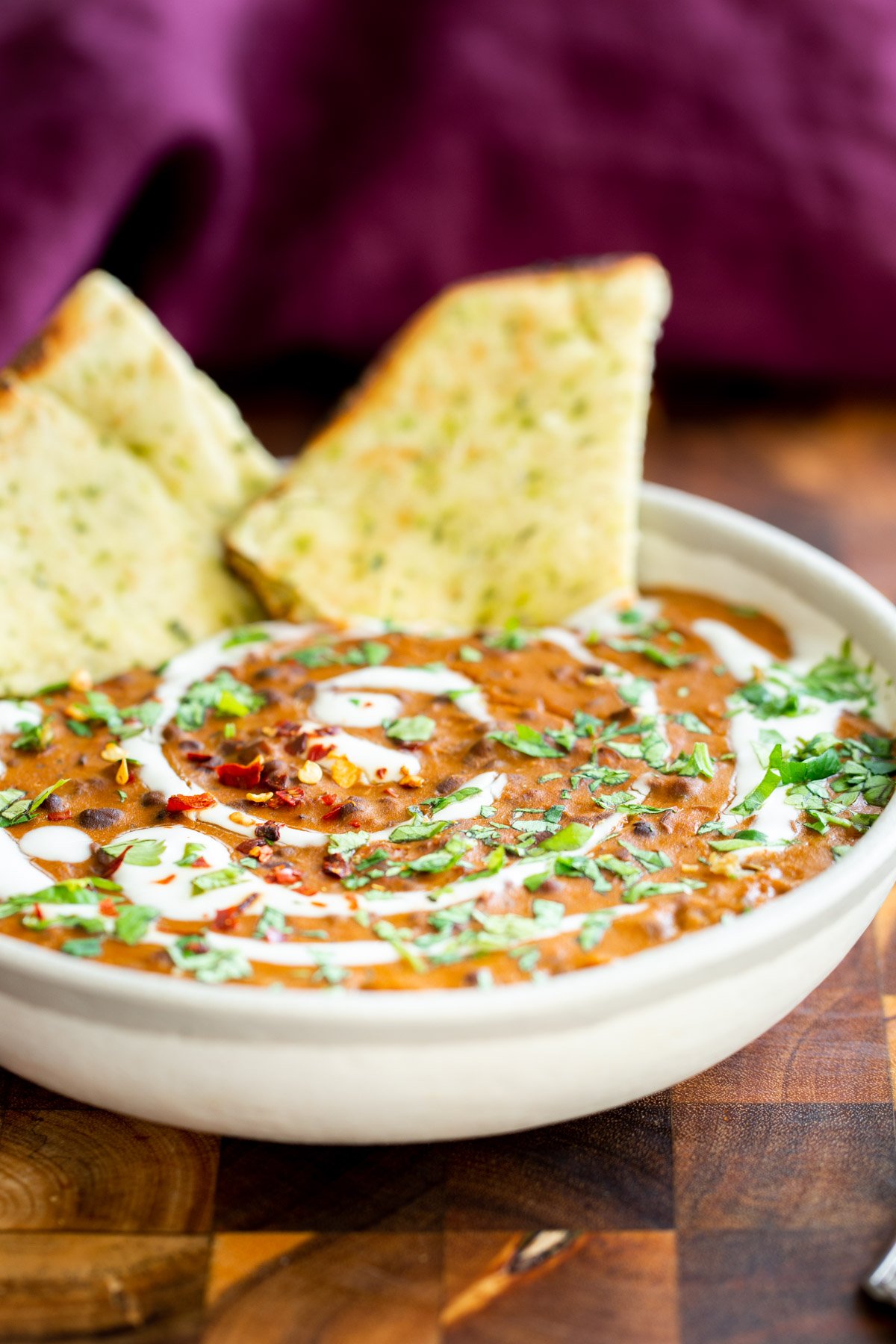 a plate of dal bukhara in a small white bowl served with naan