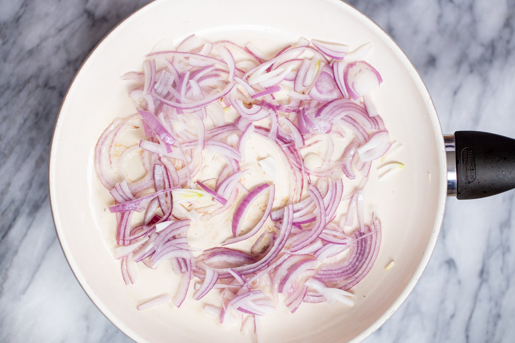 sliced red onions in a white sauteeing pan