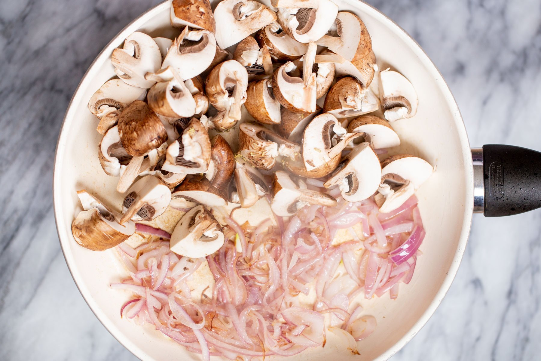 mushrooms and onions in a white sauteeing pan