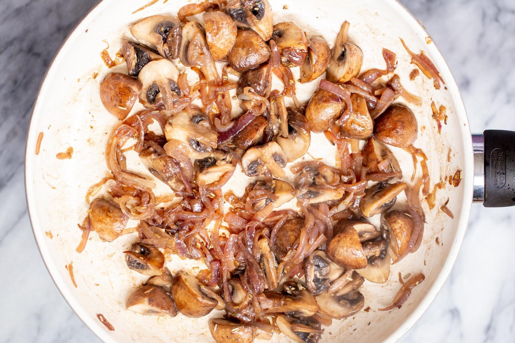 mushrooms and onions in a white sauteeing pan