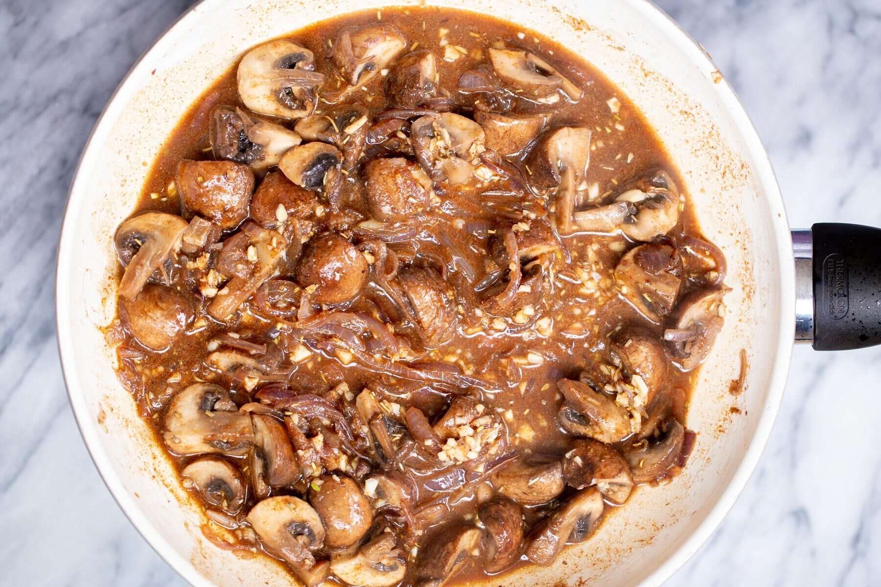 mushrooms simmering in a white sauteeing pan