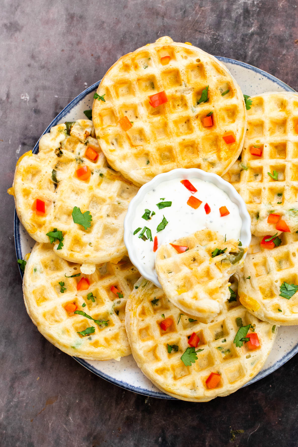 a plate of vegan savory jalapeno cheddar waffles with a dip in the middle and a piece of waffle dipped in the dip dish