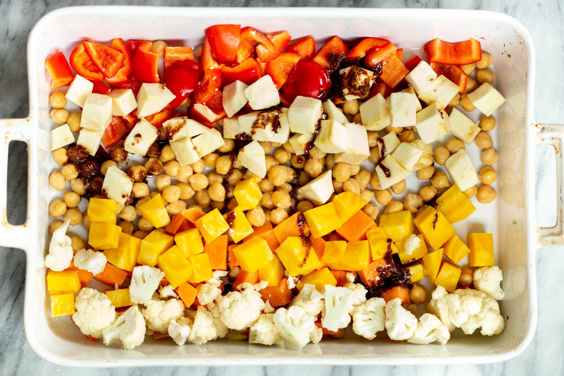 maple syrup and balsamic vinegar being drizzled over chopped veggies in casserole dish