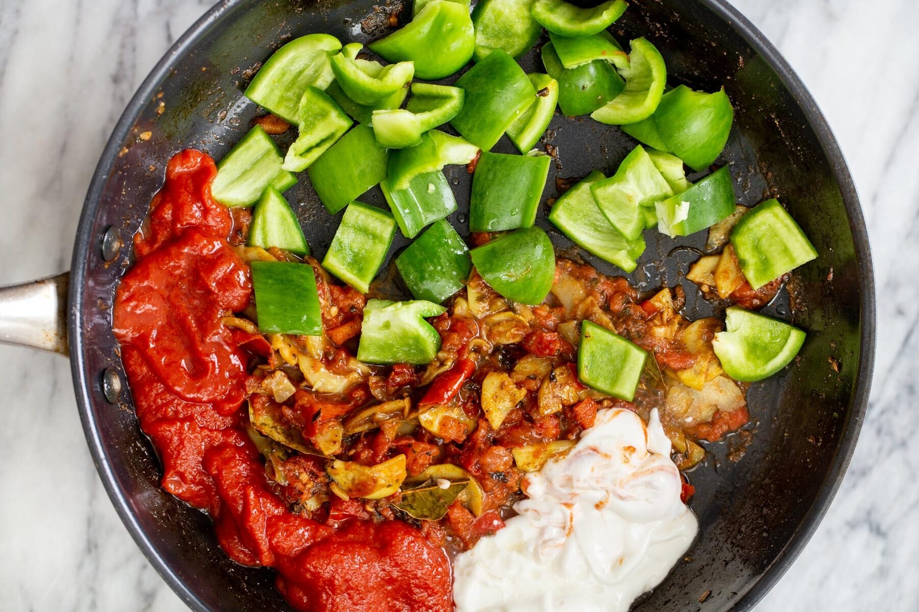 green bell pepper being added to pan with spice paste, yogurt and tomato to make tikka masala