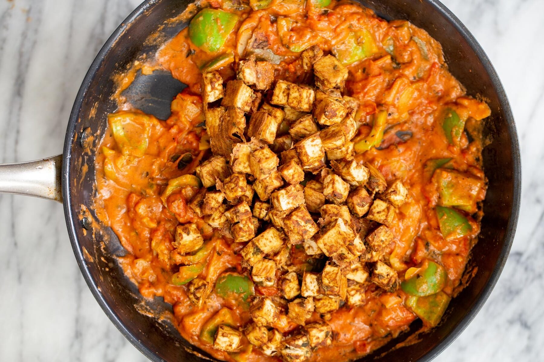 baked tofu chunks being added to frying pan with masala