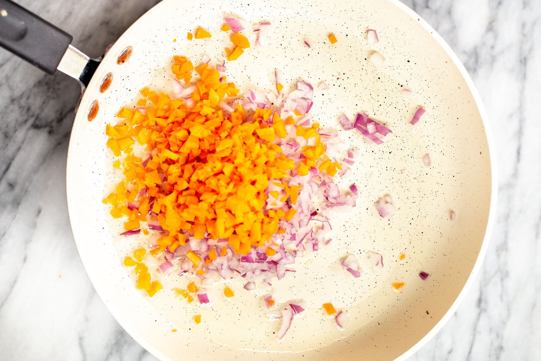 chopped carrots and onions in a sauteeing pan