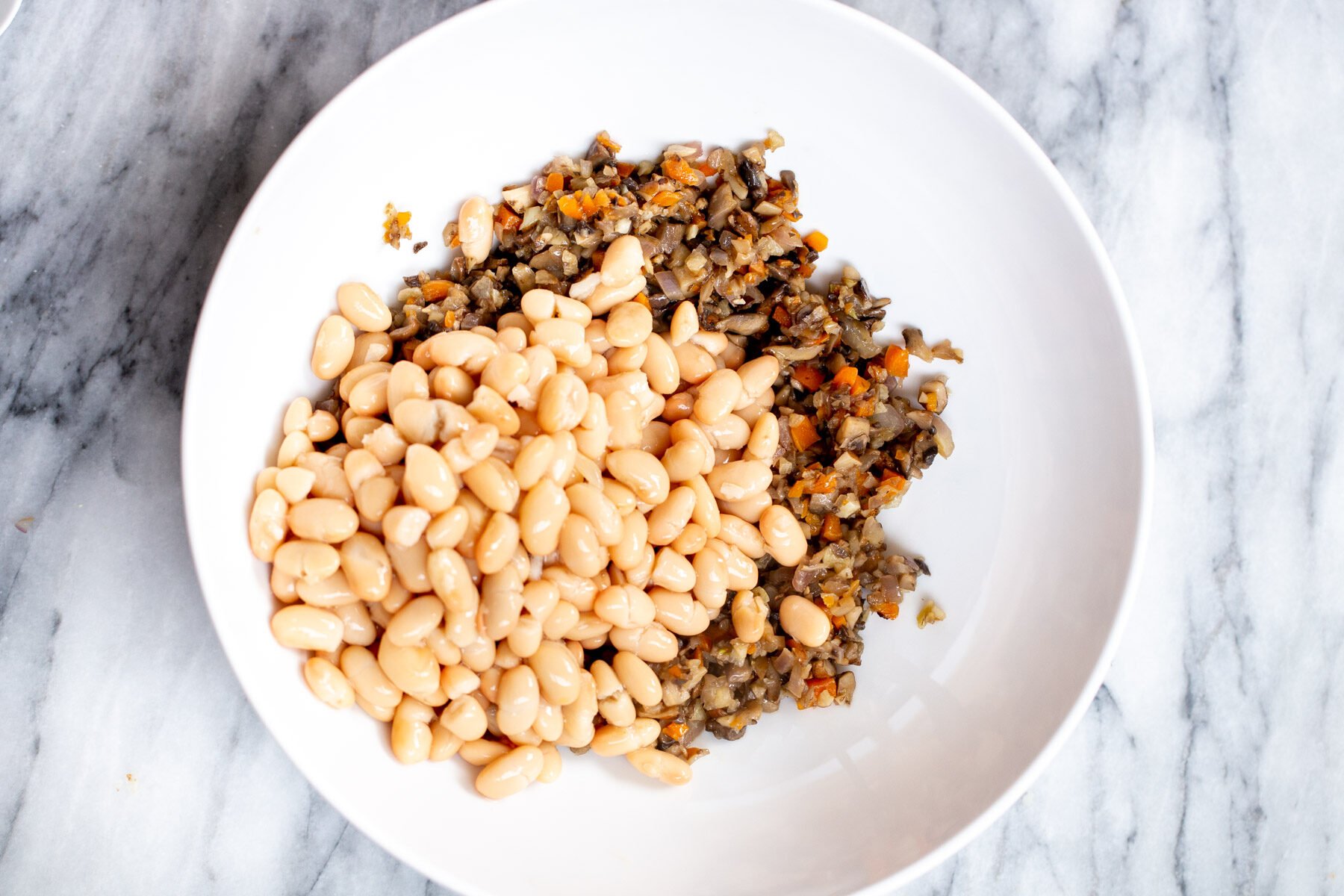 white beans being added to sauteed veggies in a pan