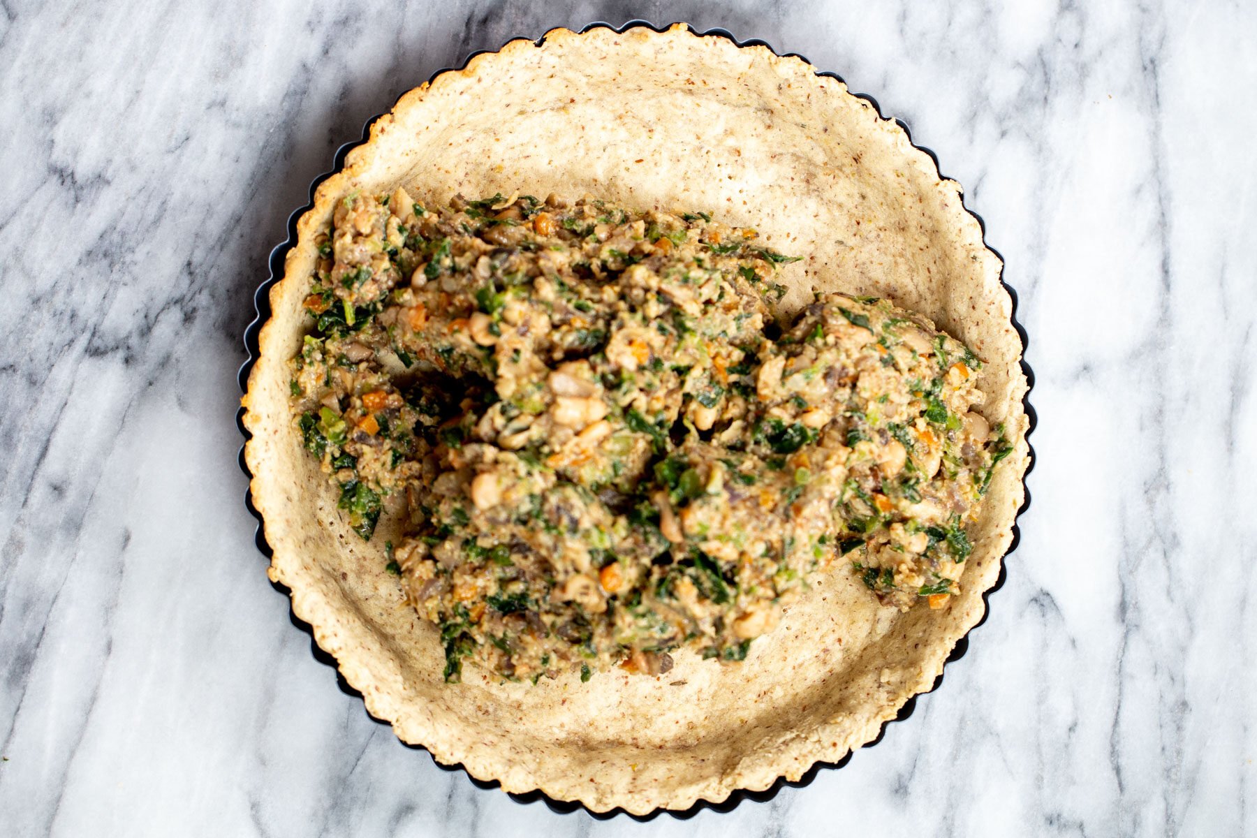 vegan spinach mushroom filling being added to savory pre-baked crust