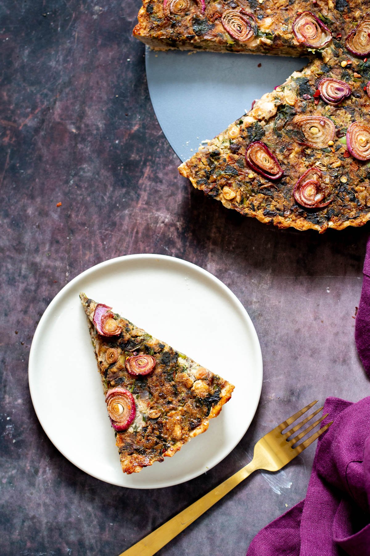 a slice of vegan mushroom tart on a white plate with a golden fork on the side