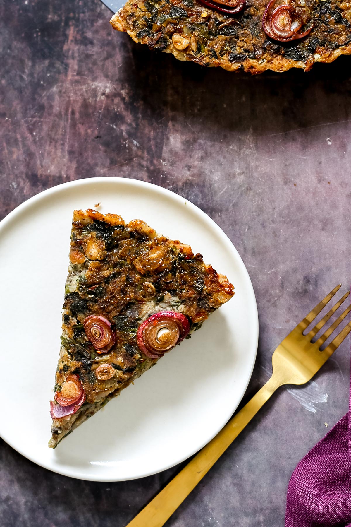 vegan mushroom tart a slice of vegan spinach mushroom tart on a white plate with a golden fork on the side