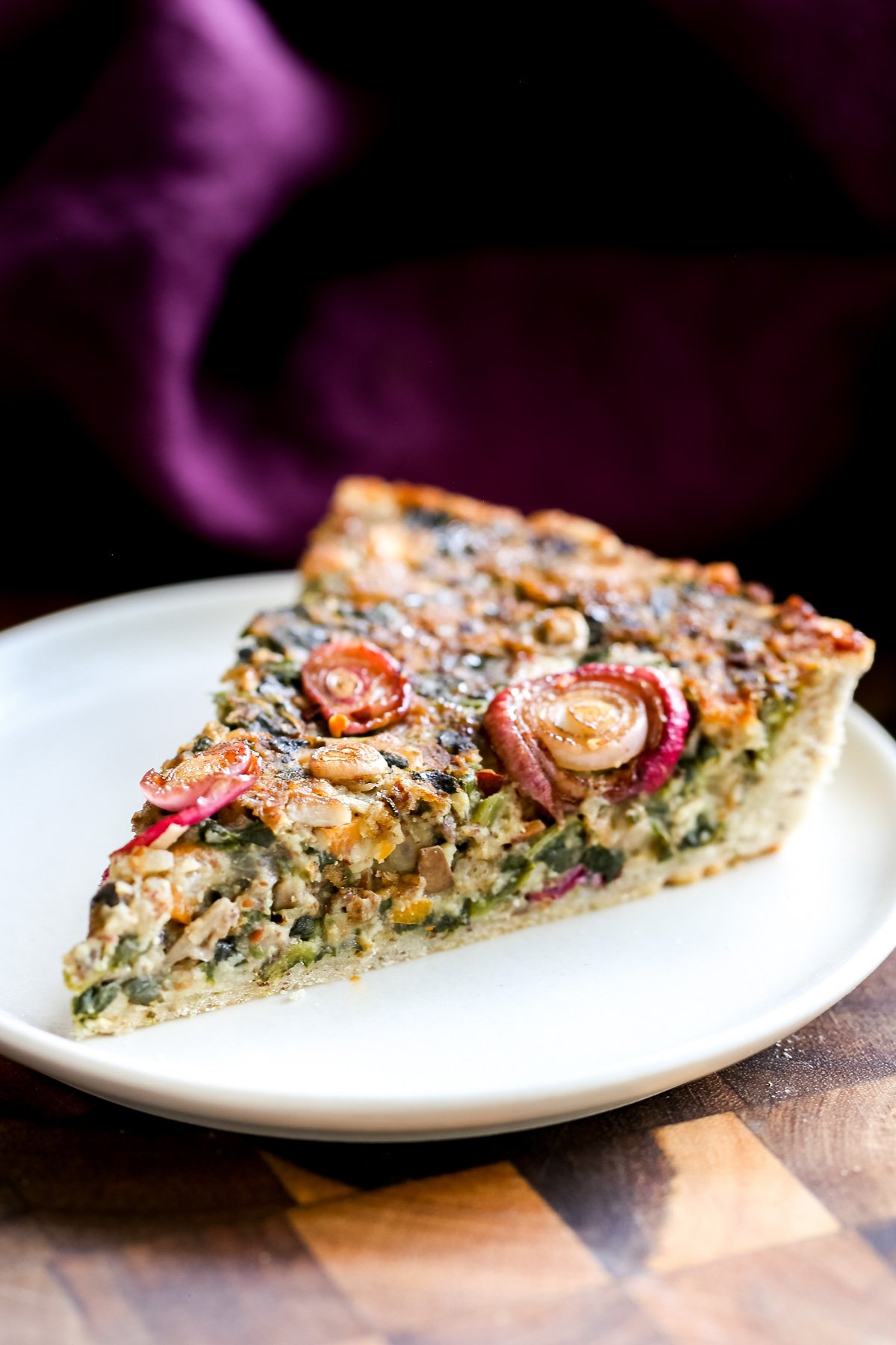 a slice of vegan spinach mushroom tart topped with sun-dried tomatoes