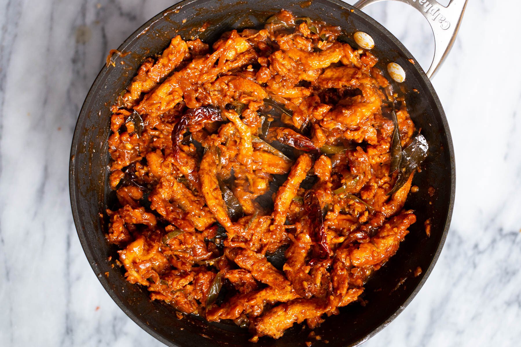 spicy baked soycurls simmering in chili marinade in a black sauteeing pan