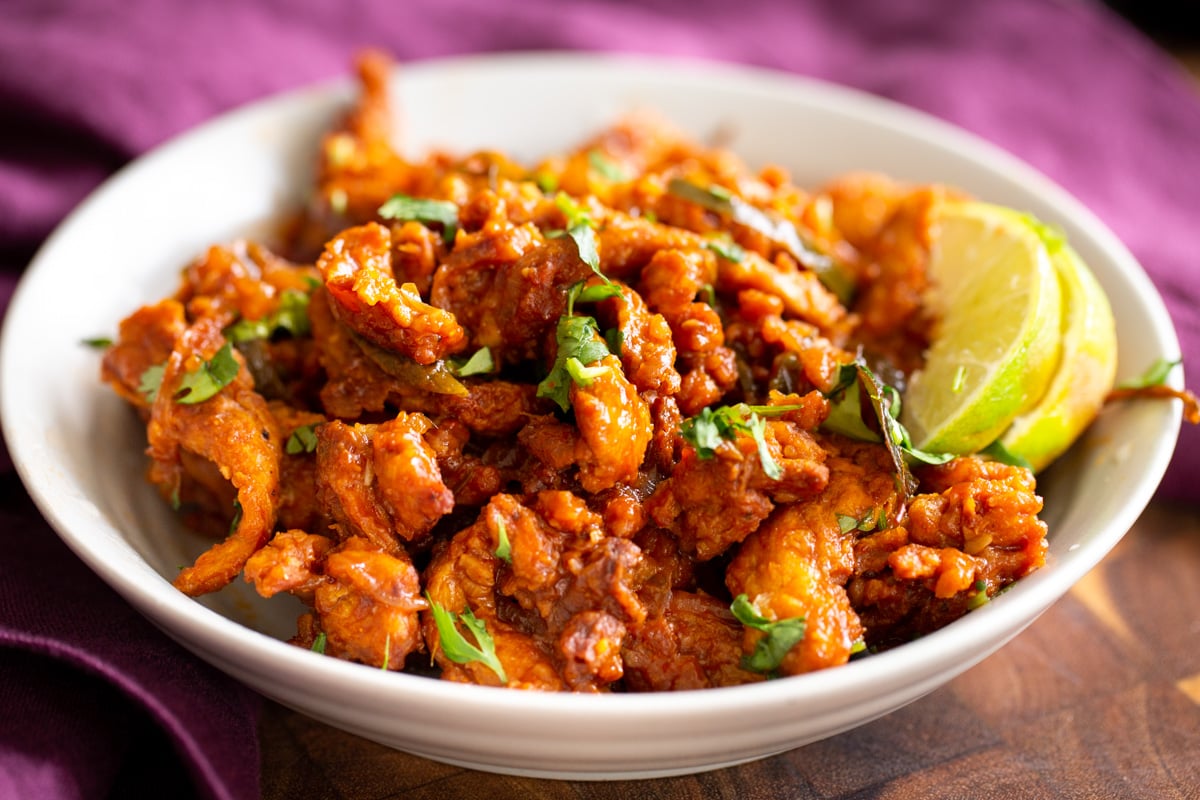 side view of a plate of vegan chicken kondattam served with lime slices