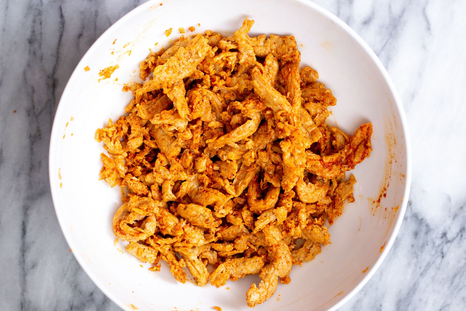 soy curls being mixed with dried spices in a white bowl