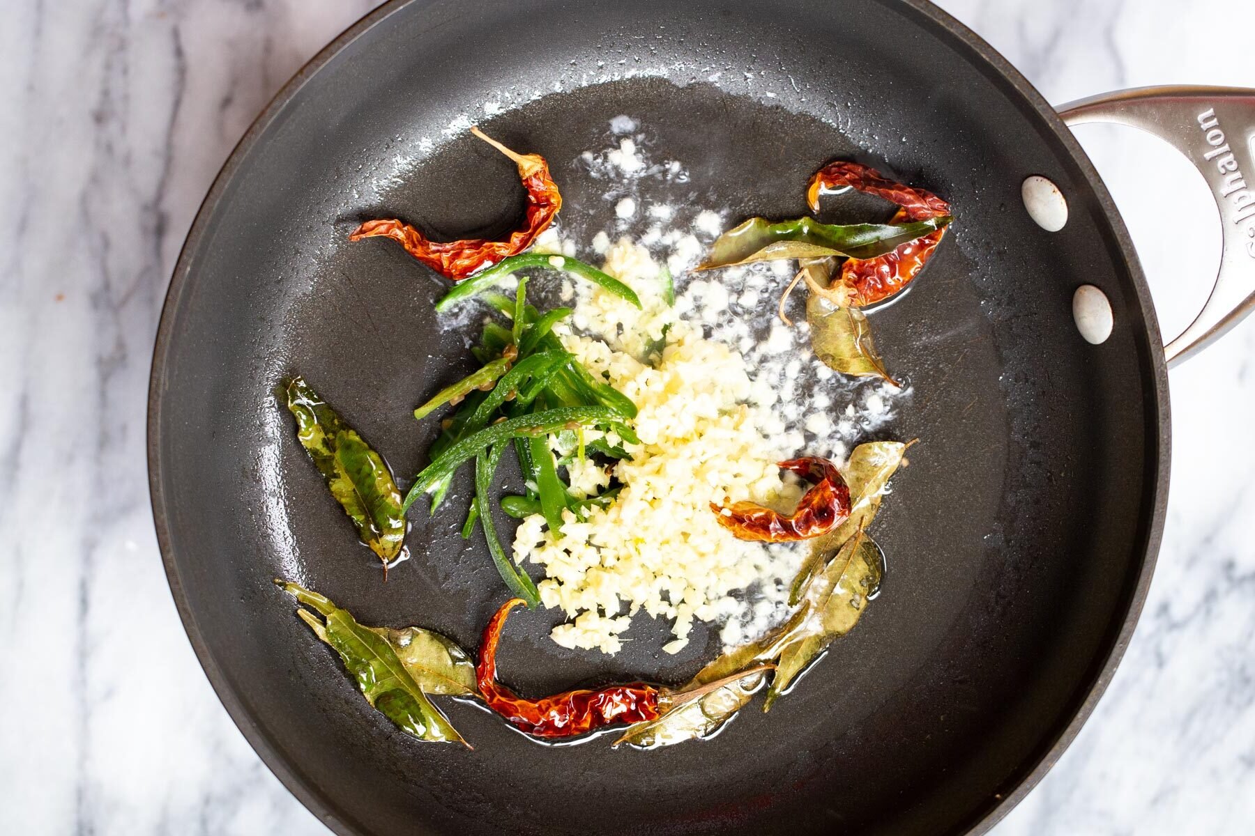 ginger, garlic, curry leaves and chilies in a black sauteeing pan