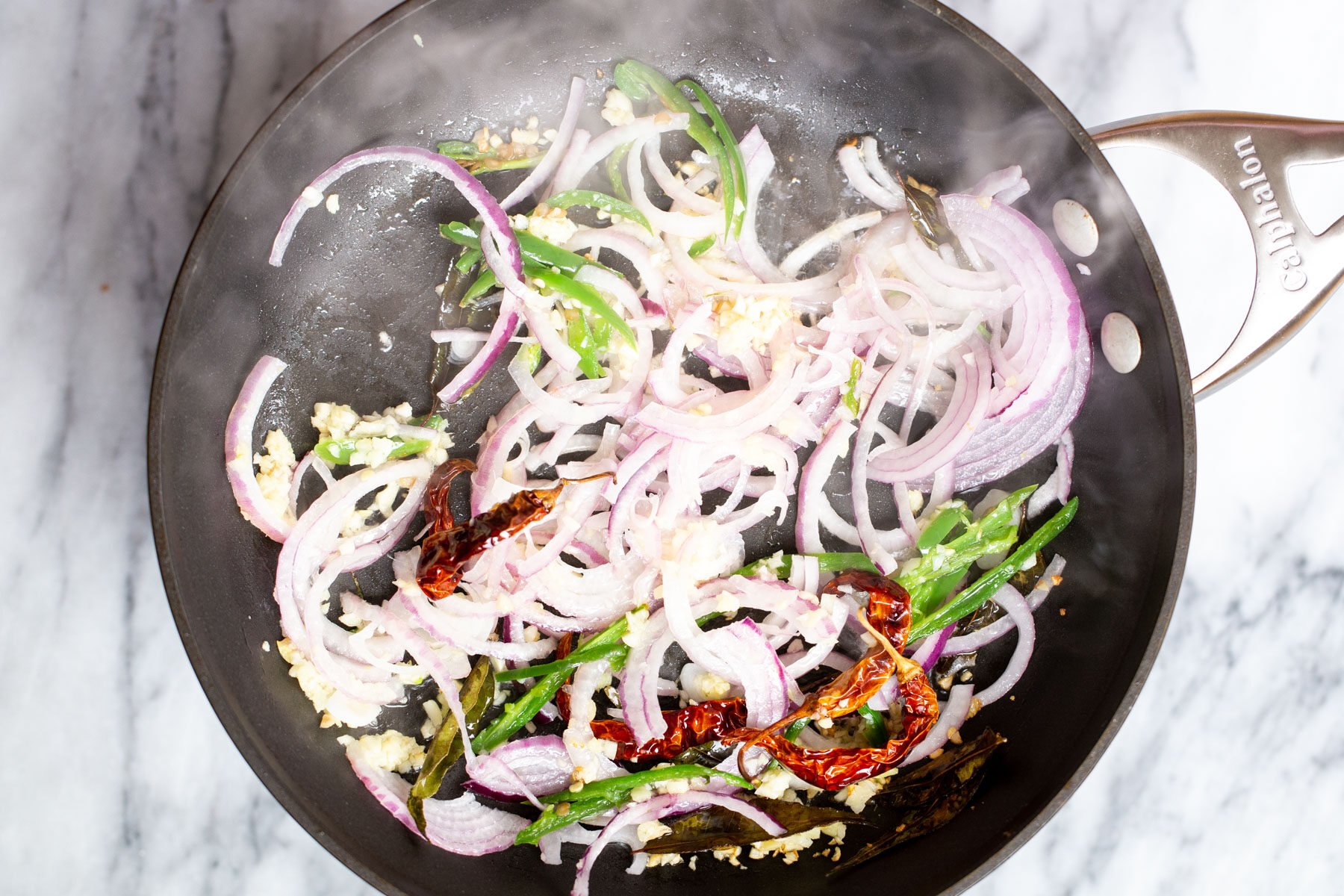 onion, ginger and garlic frying in a sauteeing pan with curry leaves and chilies