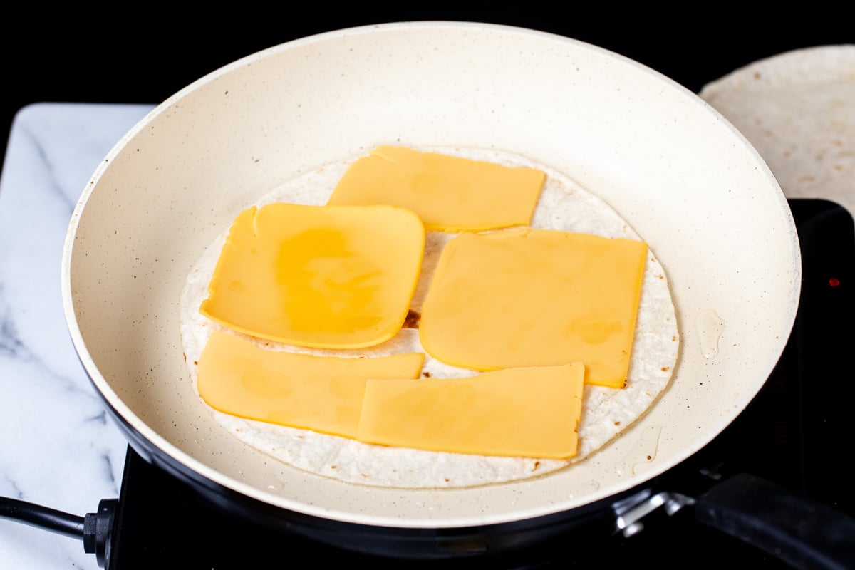 vegan cheese slices being added on top of wheat tortilla in pan