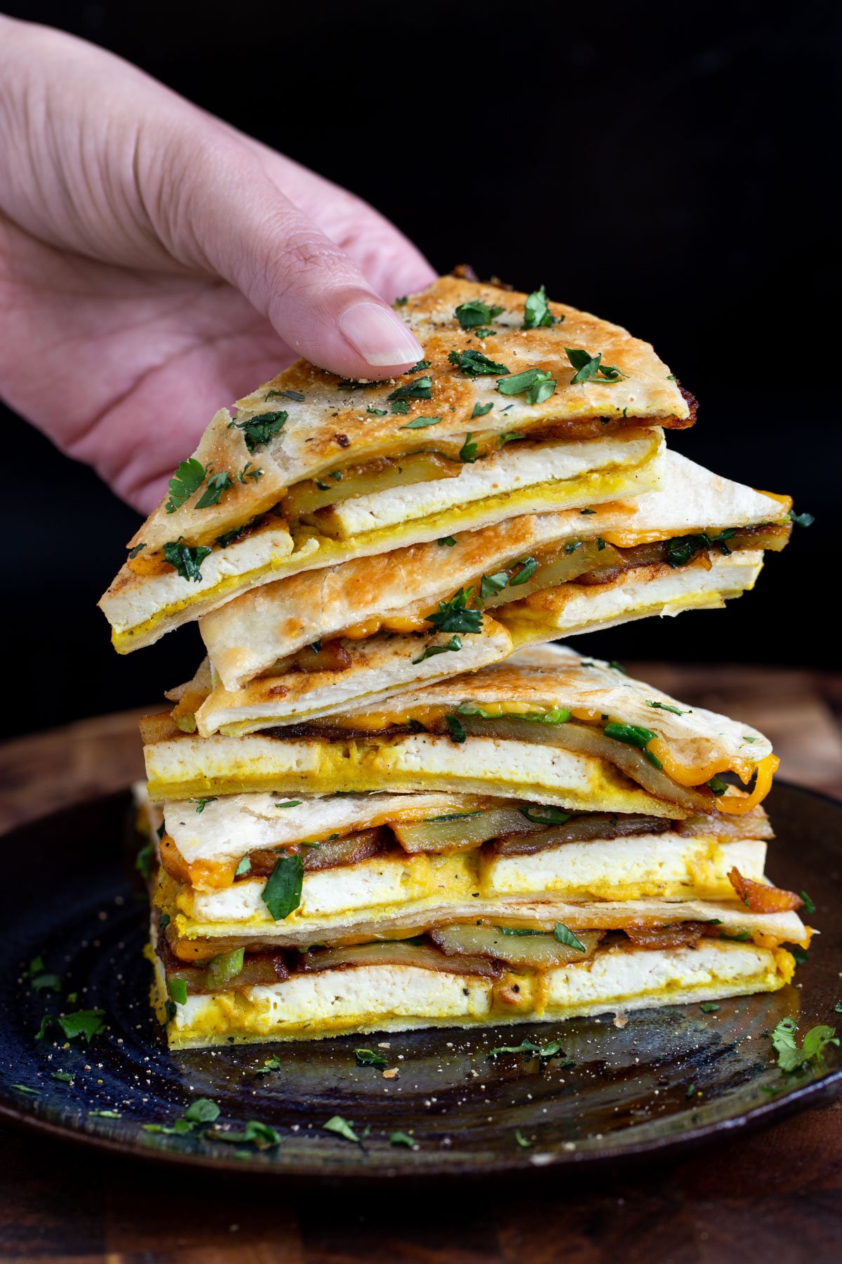 a hand reaching for a wedge of vegan breakfast quesadilla