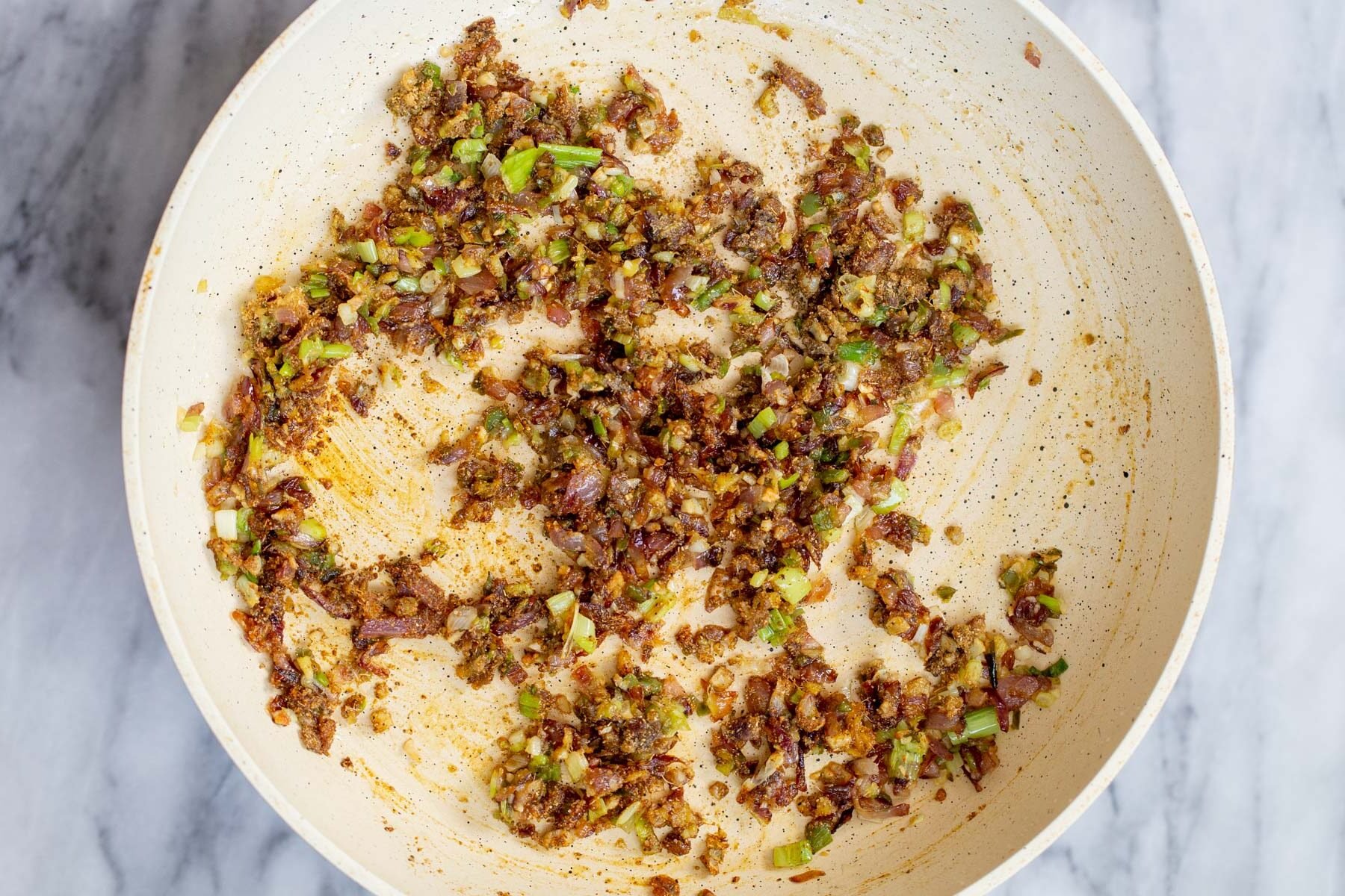 garlic, onion and green chilies in a white sauteeing pan