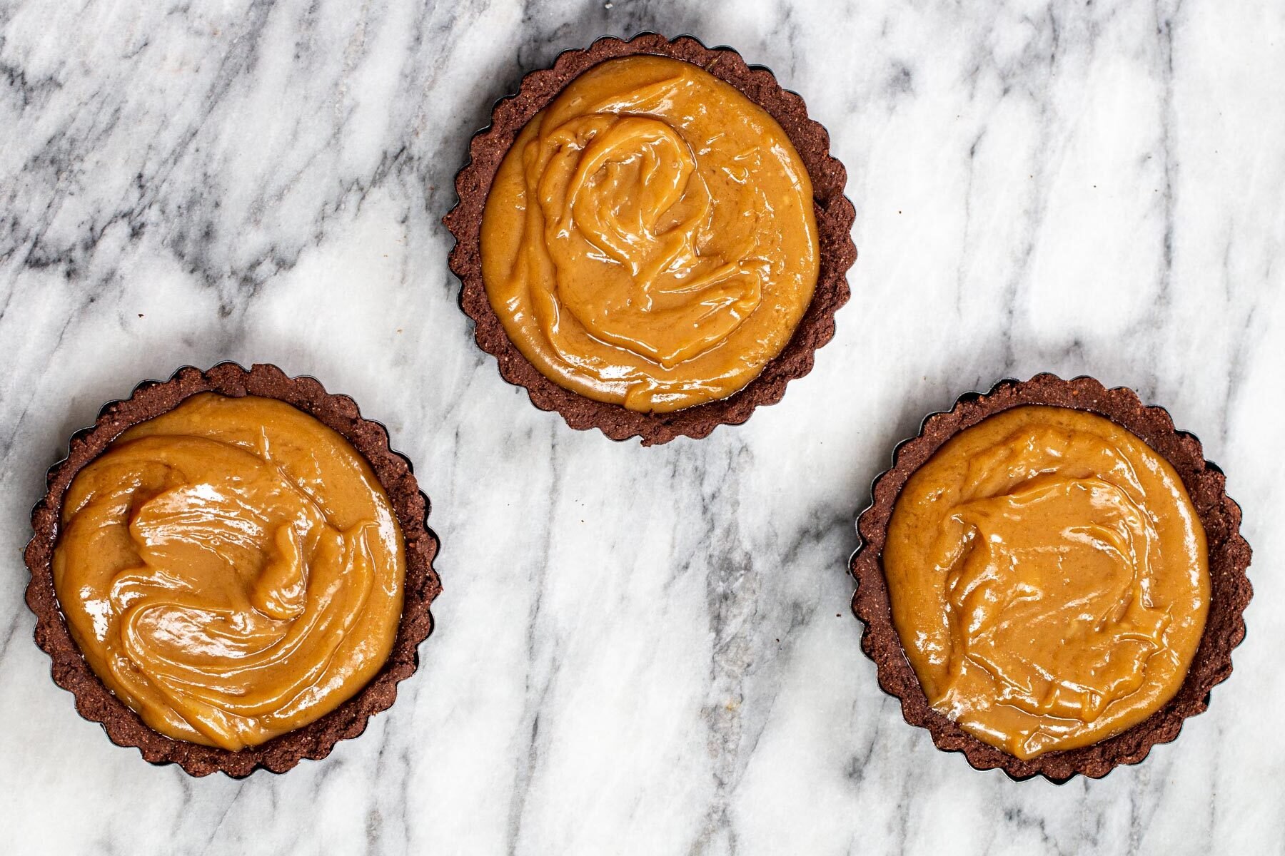 peanut butter filling being spread into chocolate tartshells 