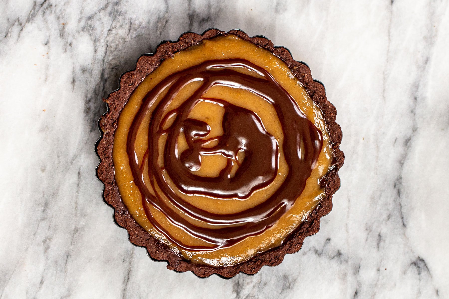 chocolate drizzle being spread over peanut butter filling in a tartshell 