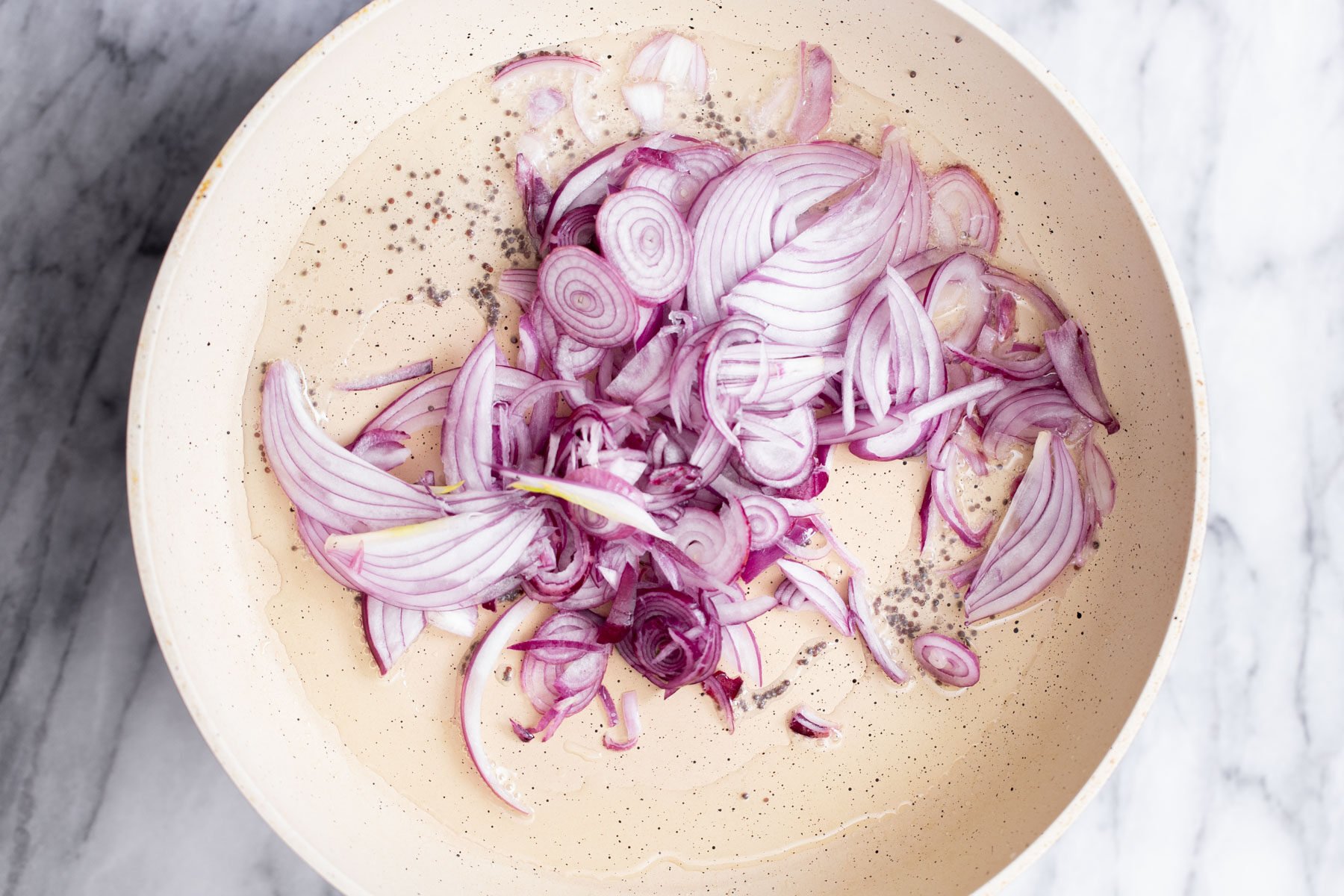 onions being added to frying pan with mustard seeds