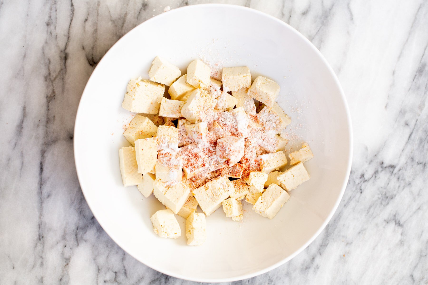 tofu cubes in a white bowl with cornstarch and spices 