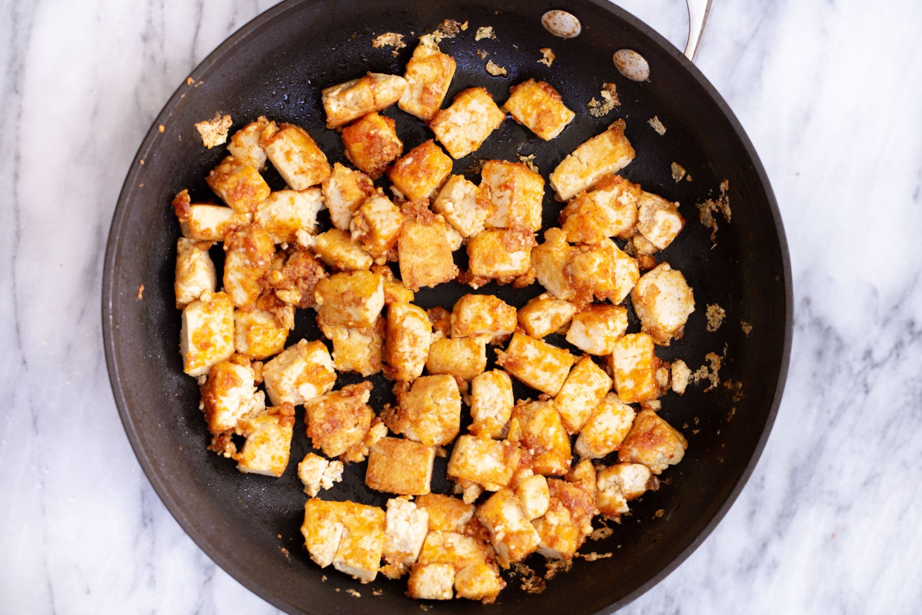 marinated tofu cubes frying in a sauteeing pan 