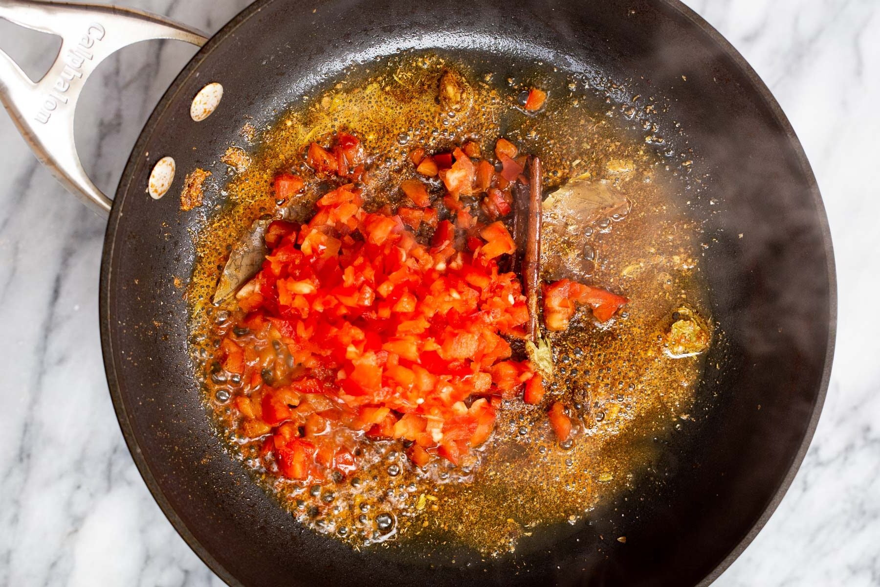chopped red bell pepper being added to hot oil in a frying pan 