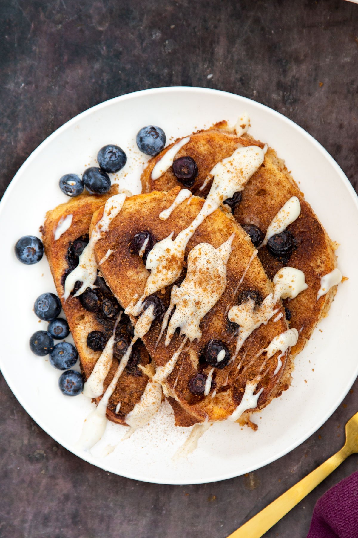 a serving of vegan baked French Toast served with fresh blueberries and drizzled with custard