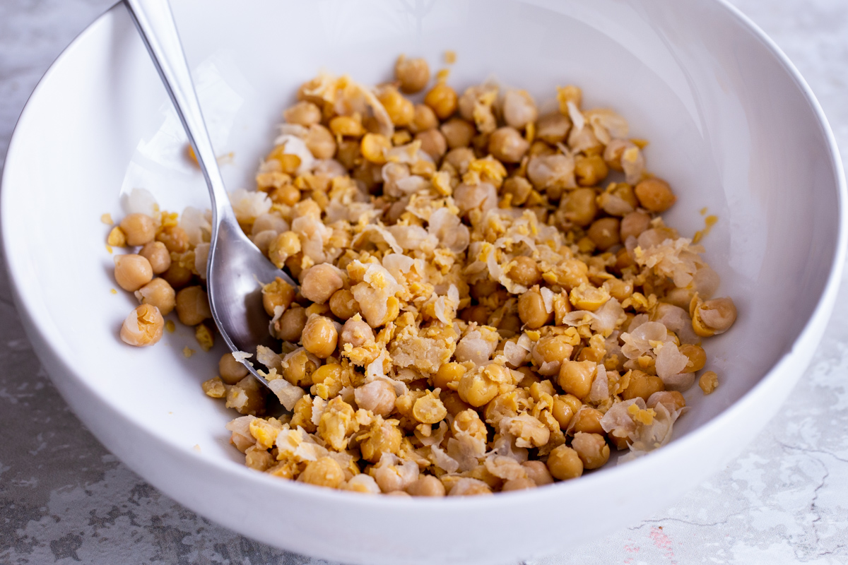 chickpeas being mashed with spices in a white bowl