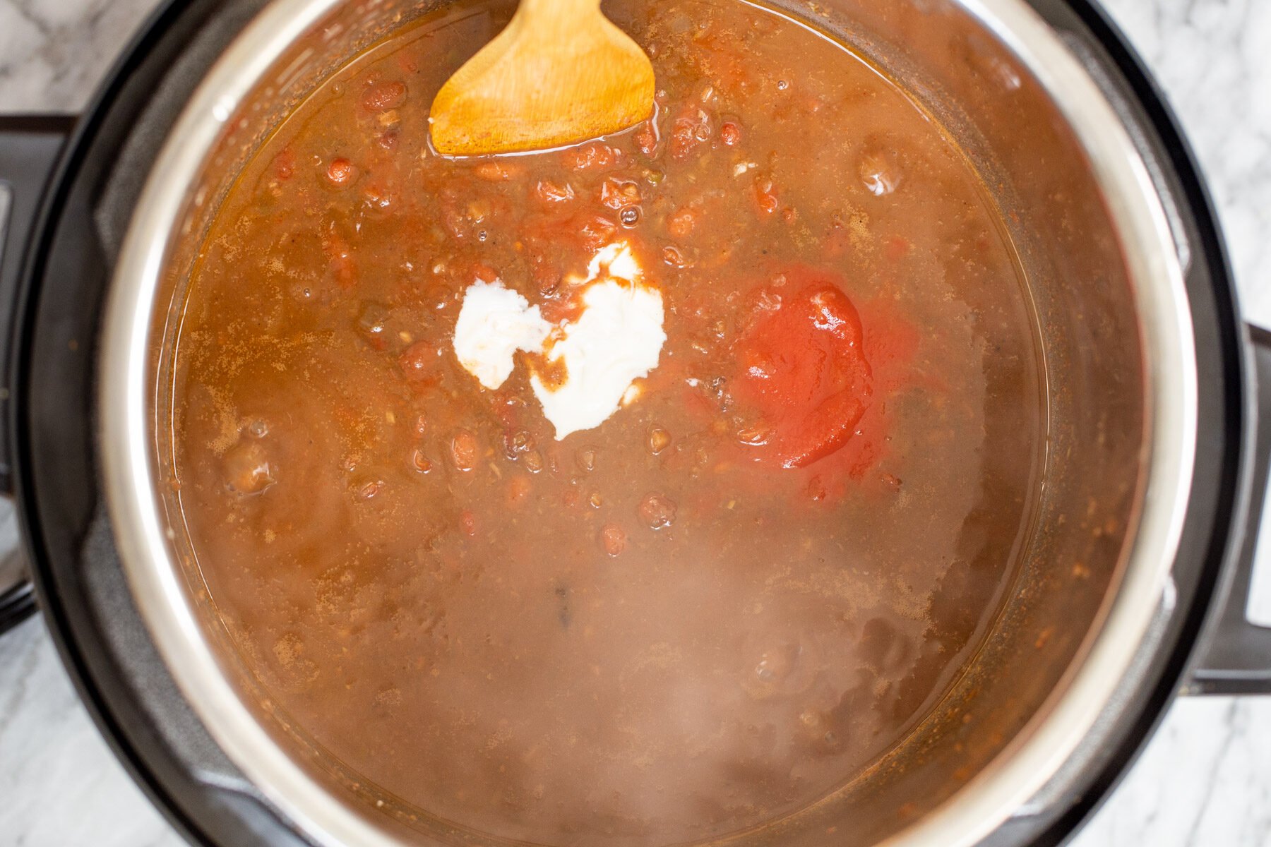 dairyfree yogurt and tomato paste being stirred into a pot with kidney bean curry