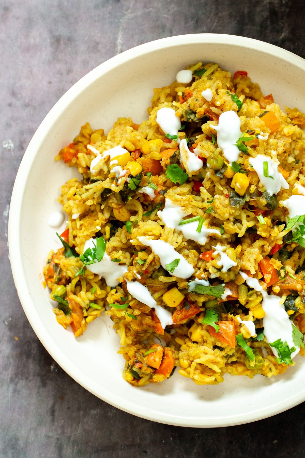close up shot of a plate of Indian lentil rice casserole drizzles with vegan yogurt