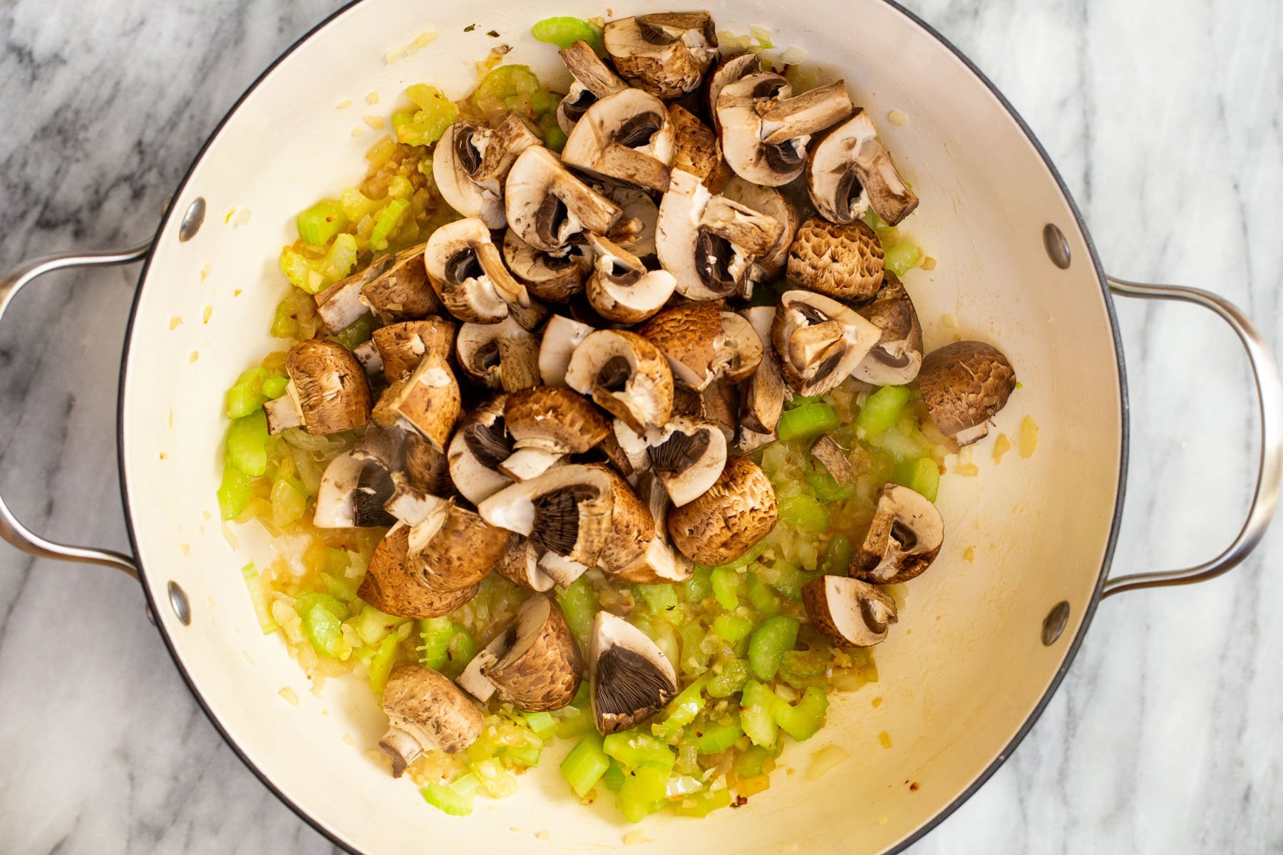 mushrooms being added to sauteed onions and garlic in a pot