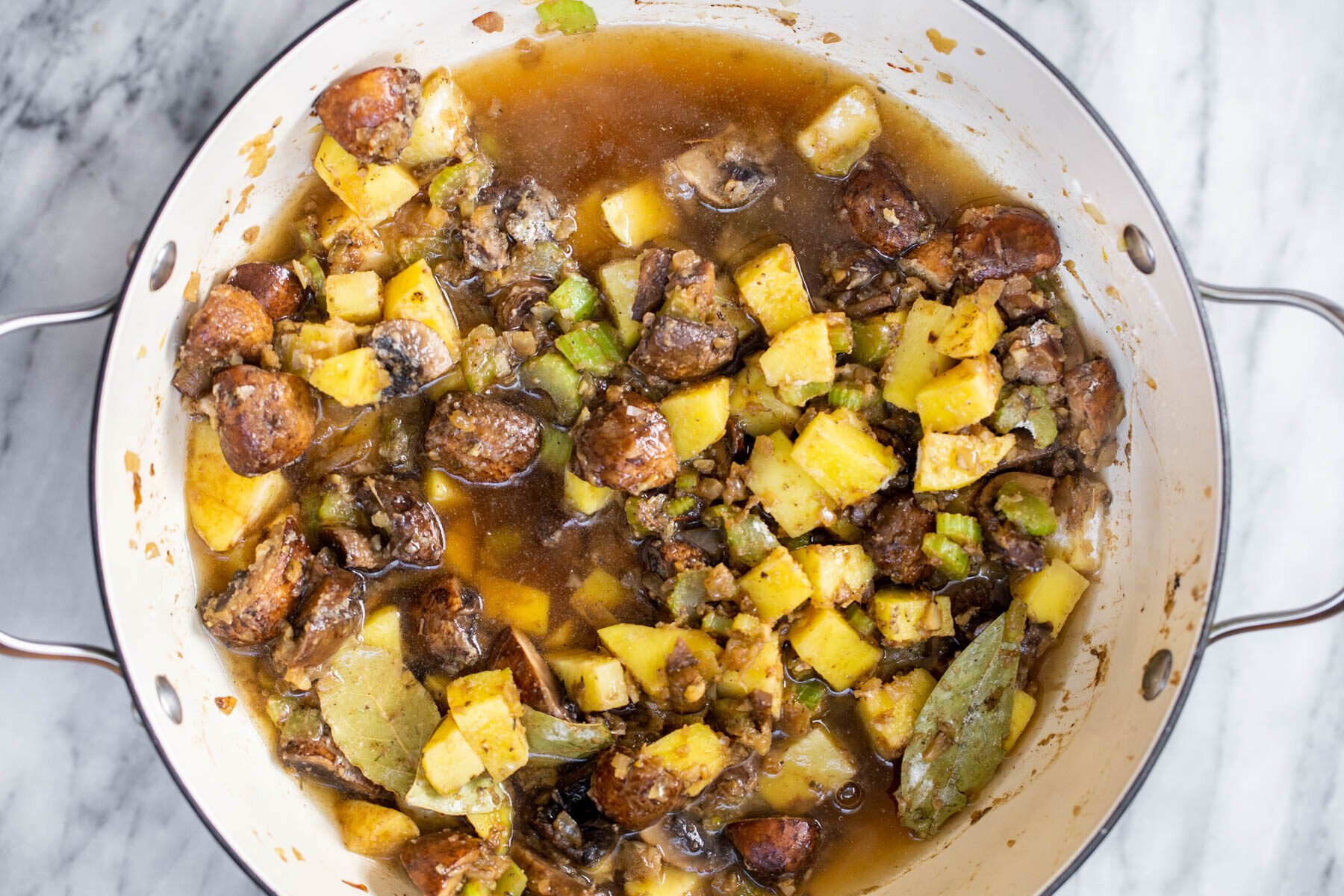 broth being added to mushrooms, potatoes and veggies in a pot to make chowder