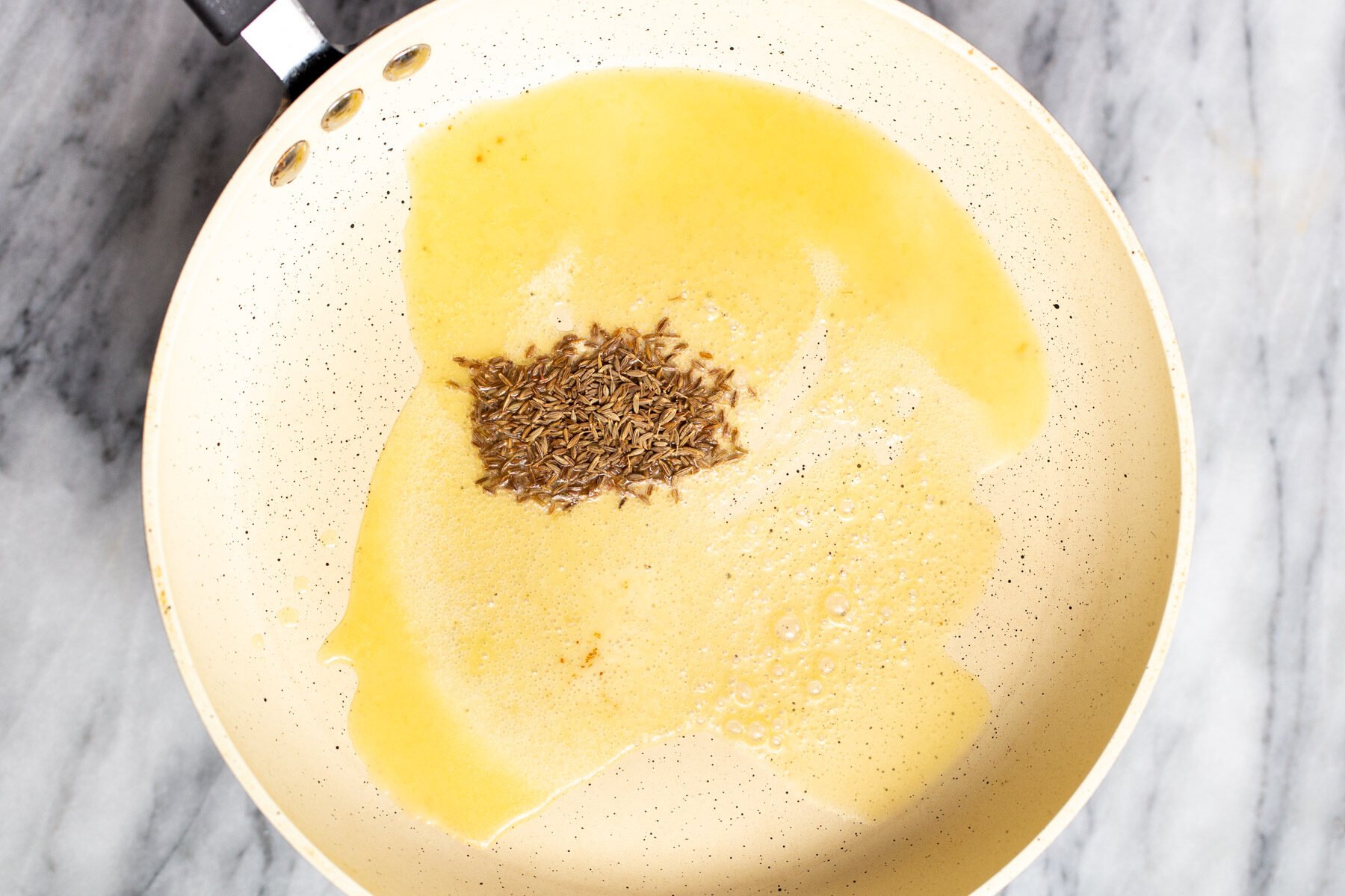 cumin seeds being fried in a frying pan 