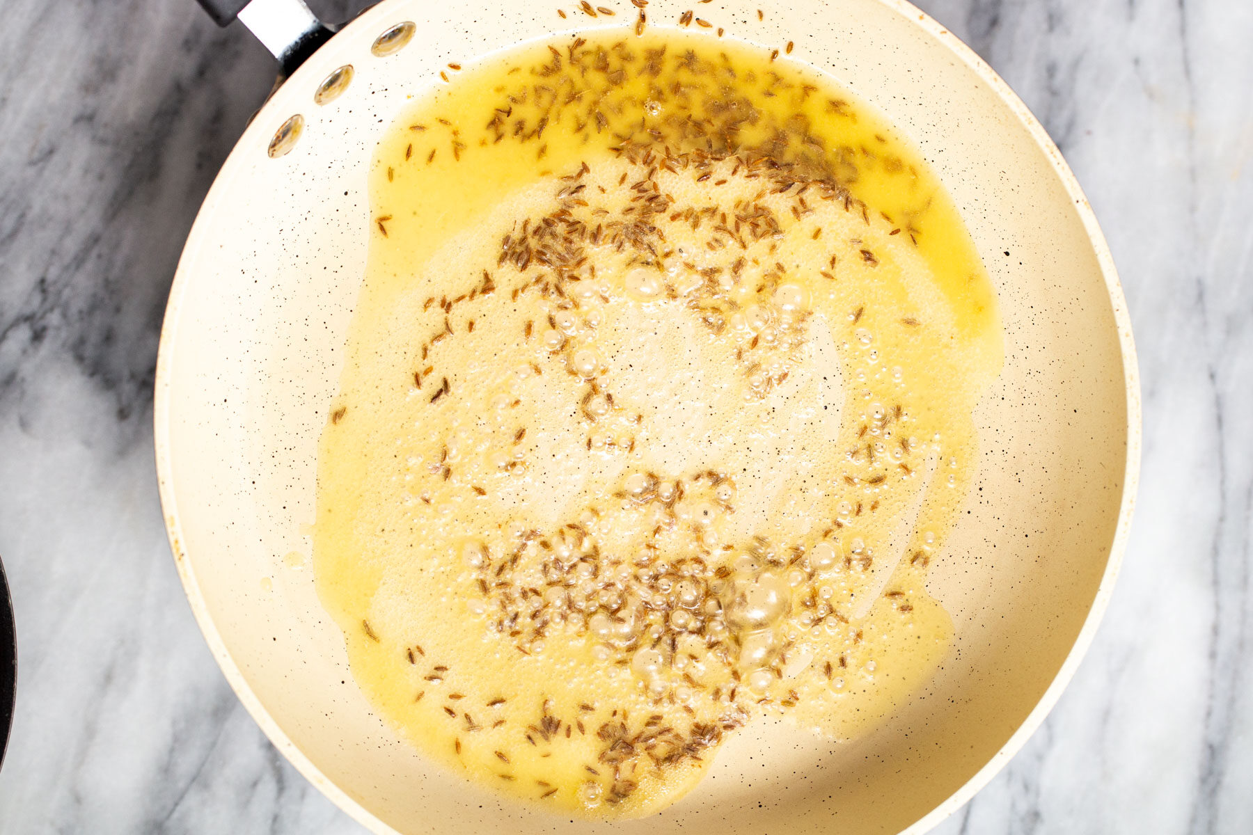 cumin seeds being fried in a pan in oil 