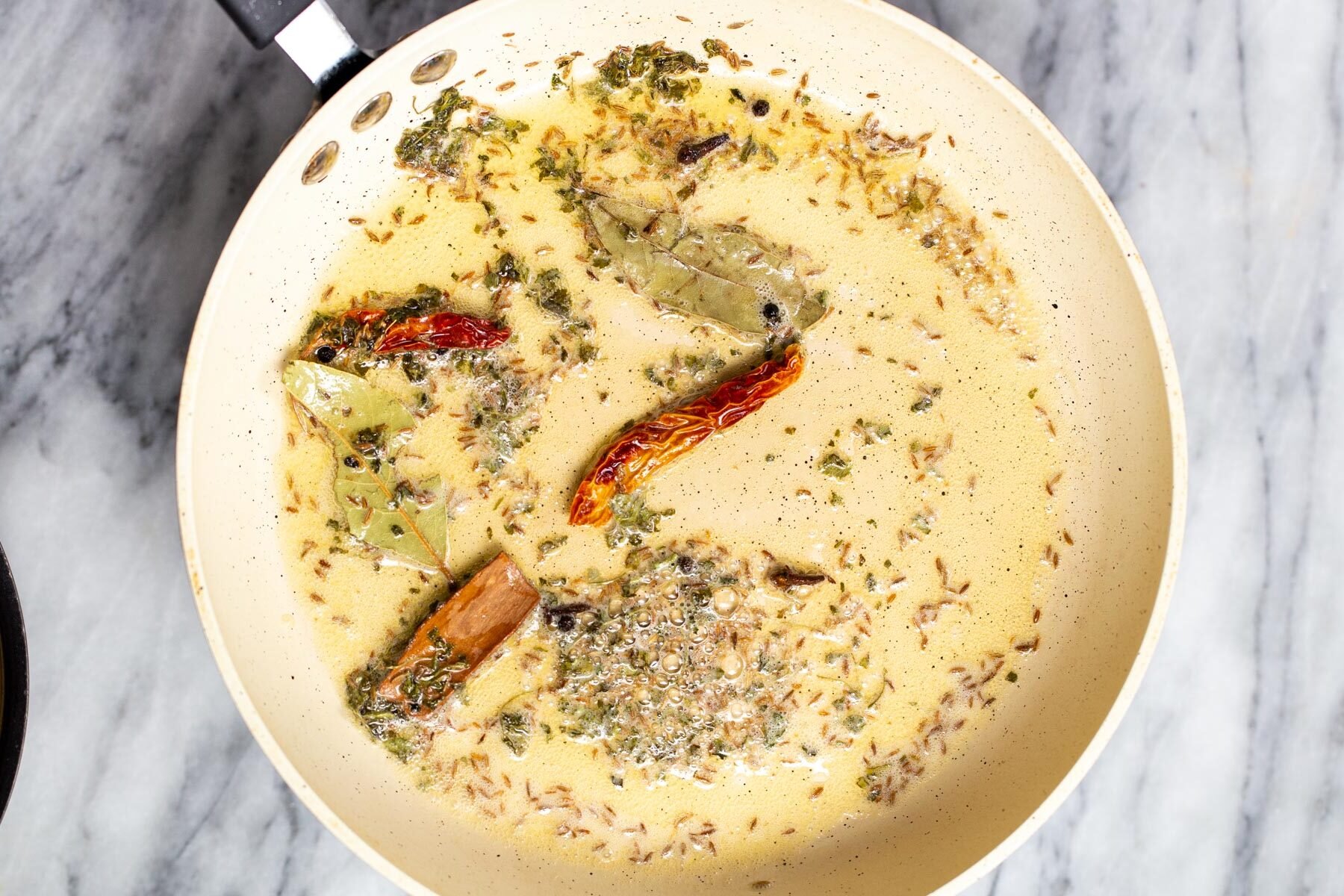 Indian tadka being prepared in a white sauteeing pan for dal recipe