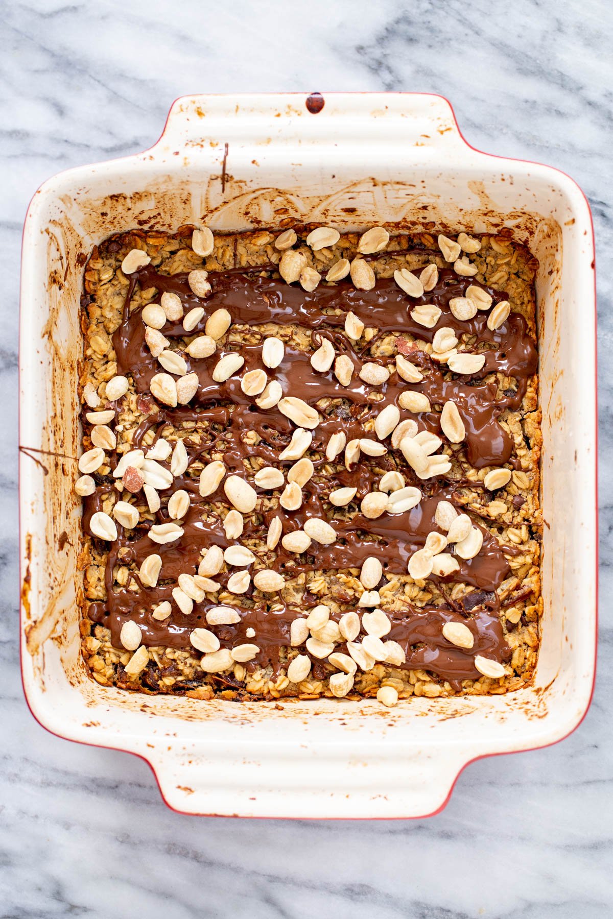 a casserole dish with peanut butter baked oatmeal topped with melted chocolate and peanuts