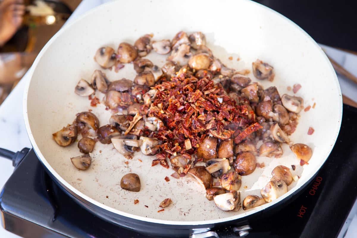 sundried tomatoes being added to a sauteeing pan with mushrooms