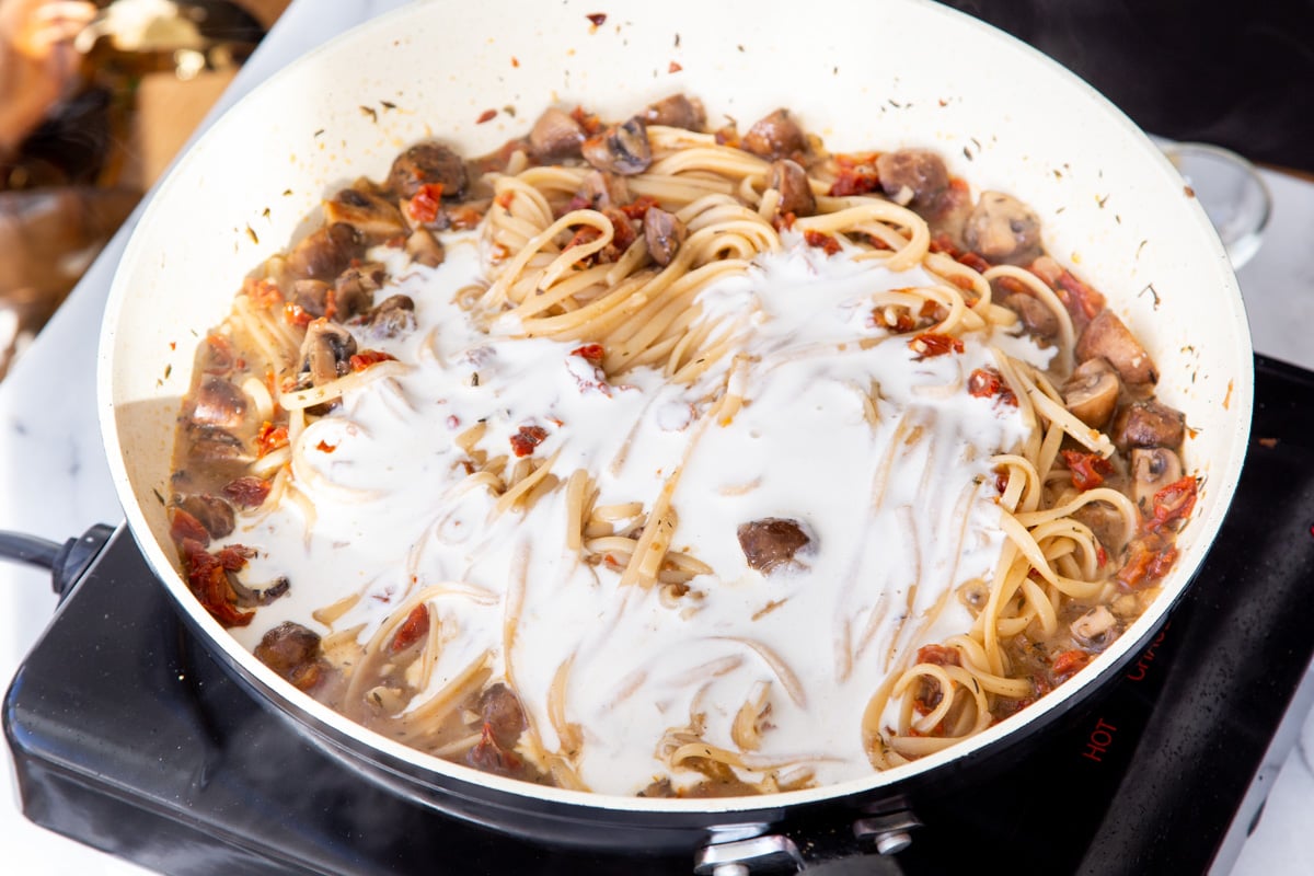 cashew cream being added to one pot mushroom sundried tomato pasta