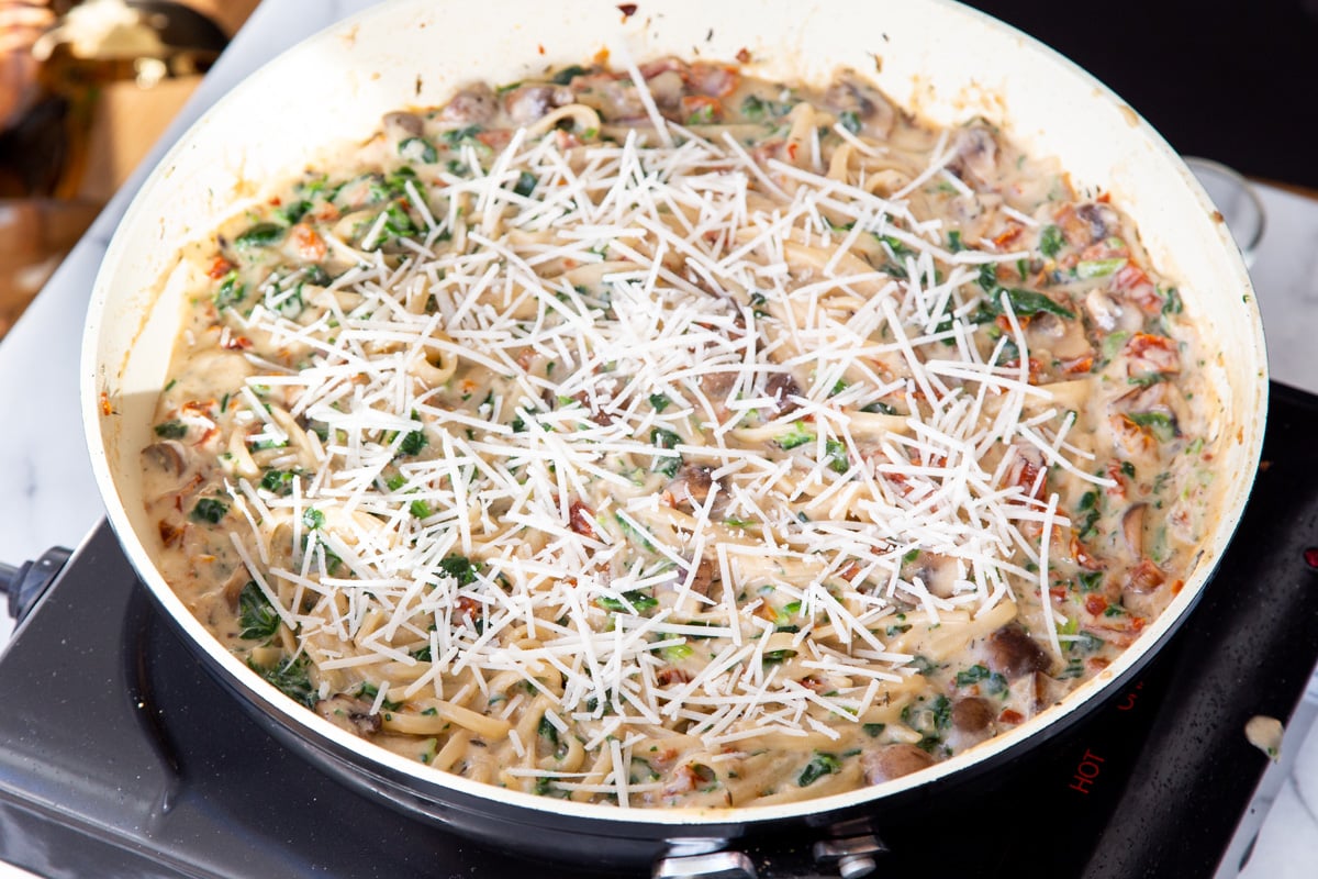 creamy spinach mushroom tomato pasta sprinkled with vegan shredded cheese