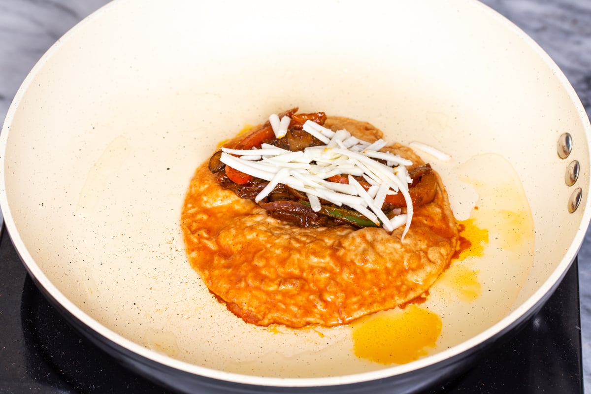 tortilla in a sauteeing pan topped with veggies and shredded cheese