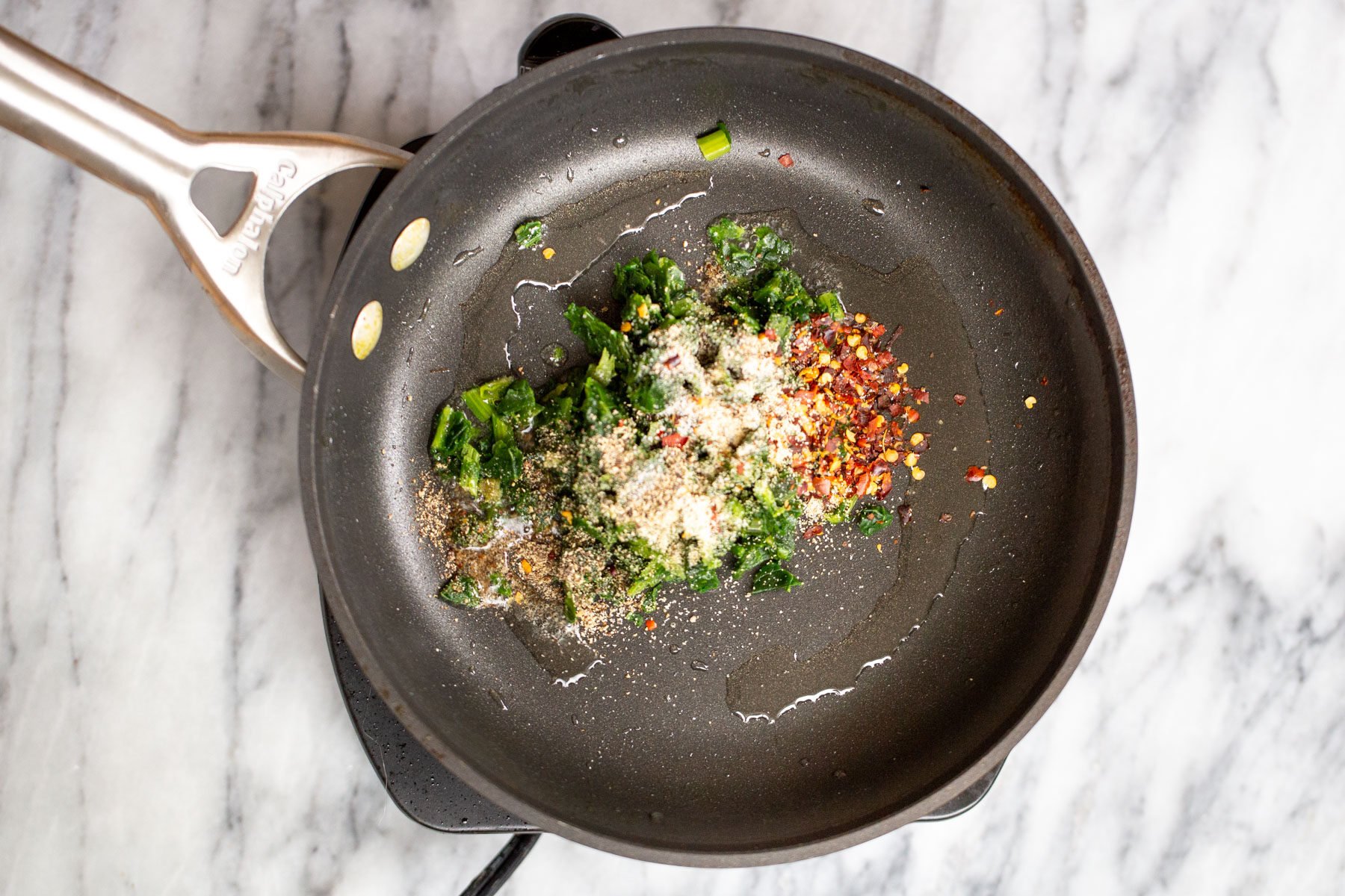 spinach, garlic and chili pepper in a black sauteeing pan