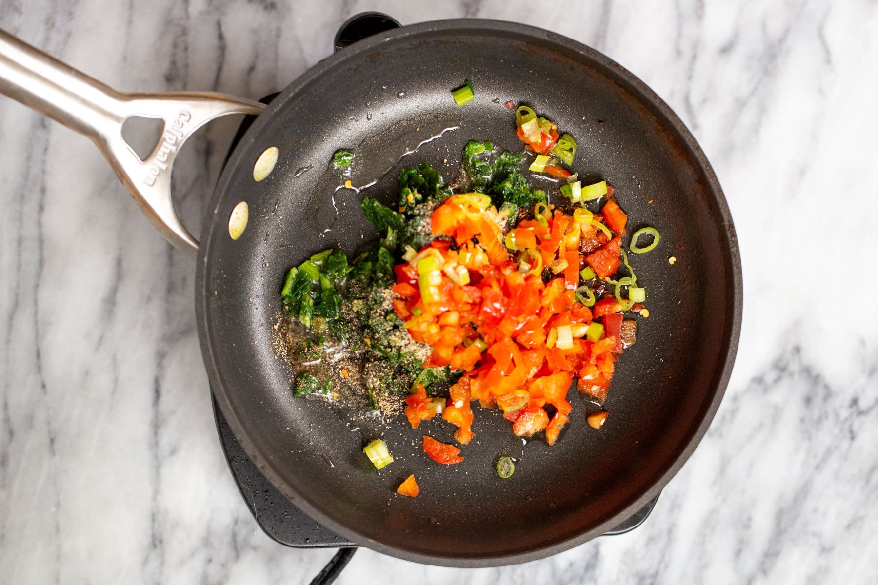 spinach and tomatoes in a black sauteeing pan