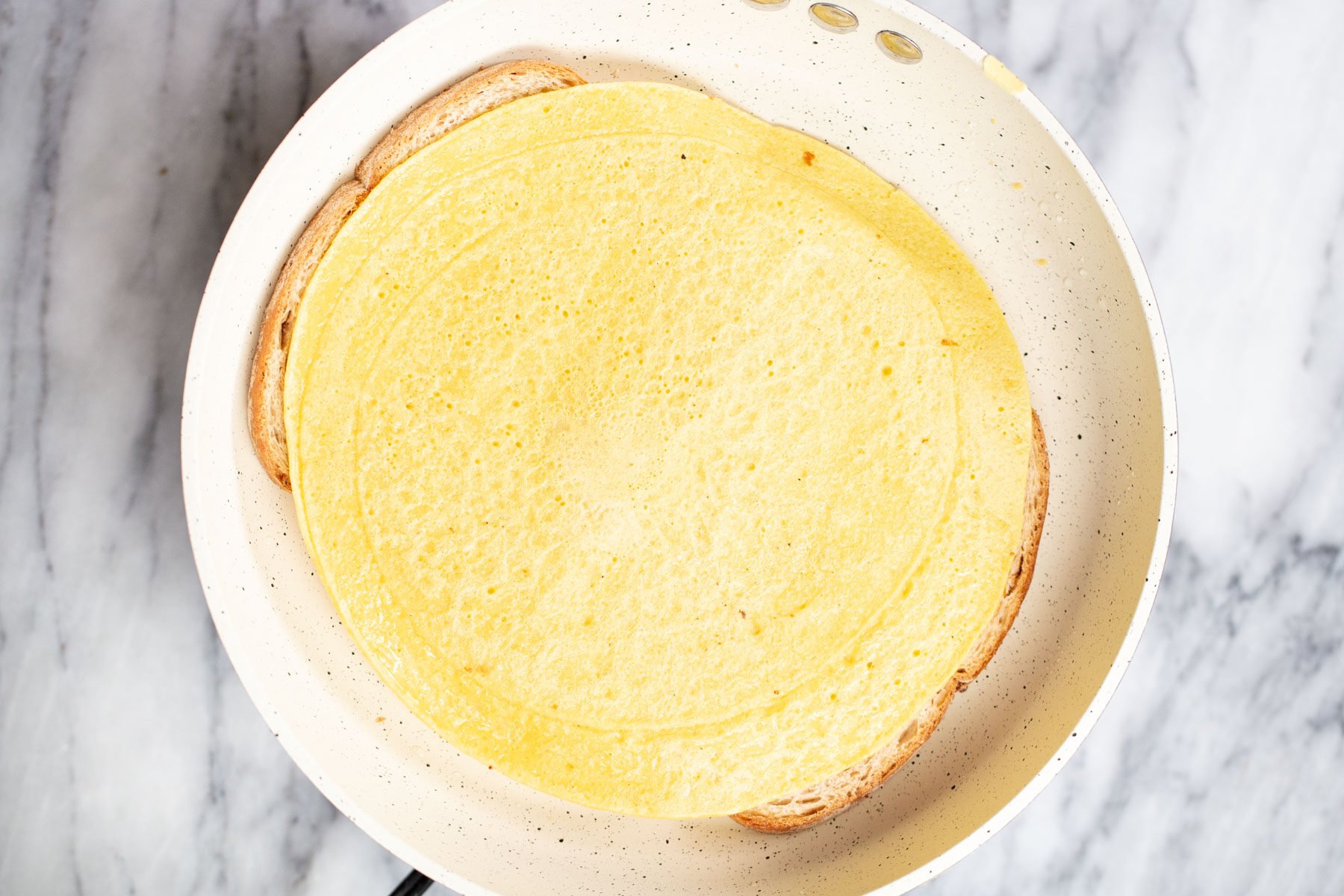 bread slices frying in a sauteeing pan topped with vegan omelette