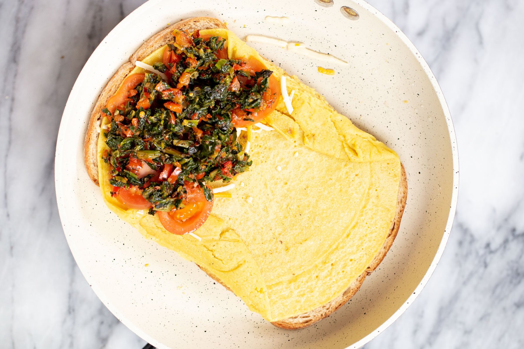 filling being added to bread slices topped with tomatoes and spinach