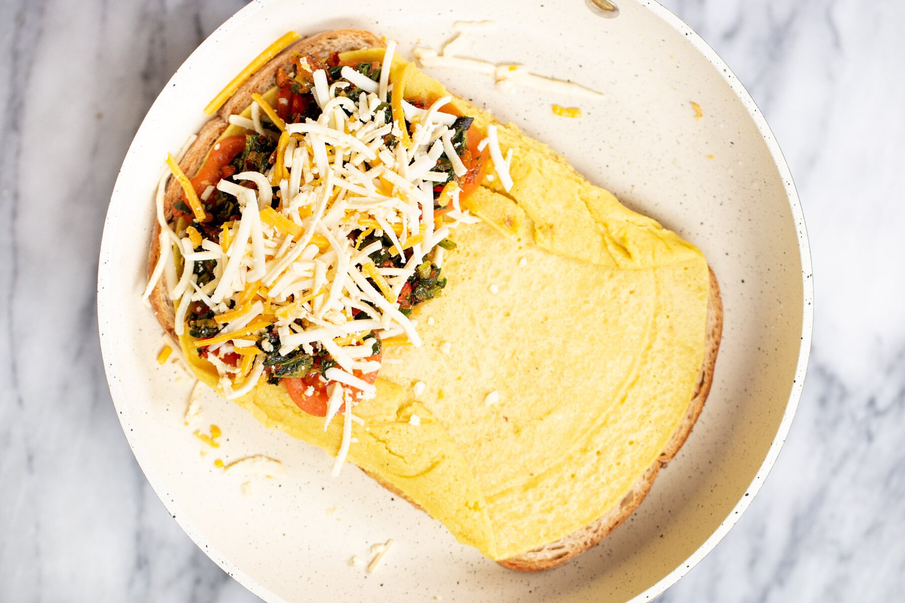 vegan omelette being topped with spinach tomatoes and cheese shreds